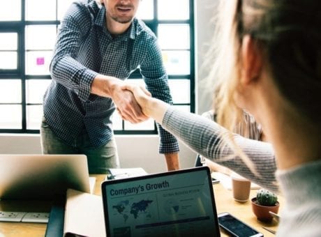 man and woman shaking hand in office with laptops
