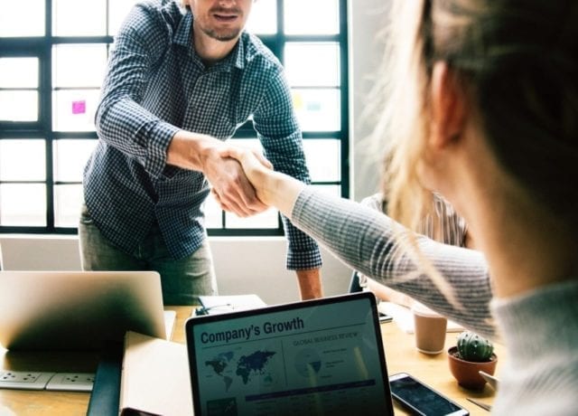 man and woman shaking hand in office with laptops